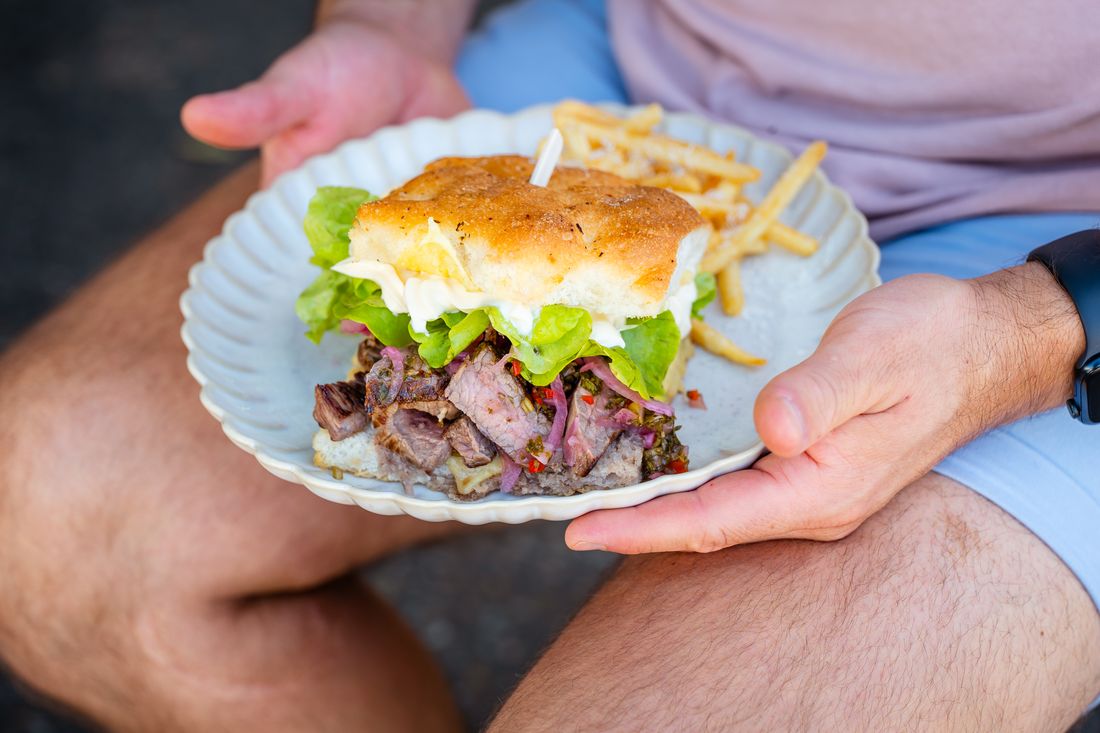 The steak sando held over a plate of french fries.
