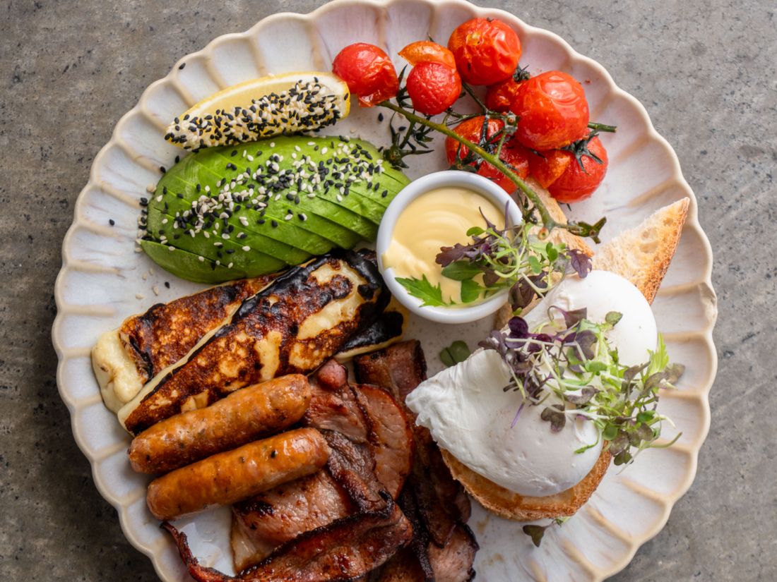 The Big Breakfast on a scalloped plate, with halloumi, chipolata sausage, bacon, truss tomatoes, avocado and a poached egg.