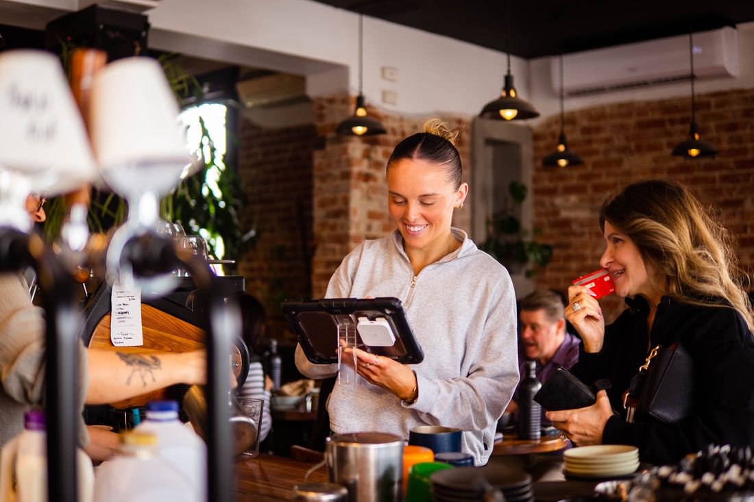 A staff member smiling behind the Cotto counter, serving customers beside the espresso machine.